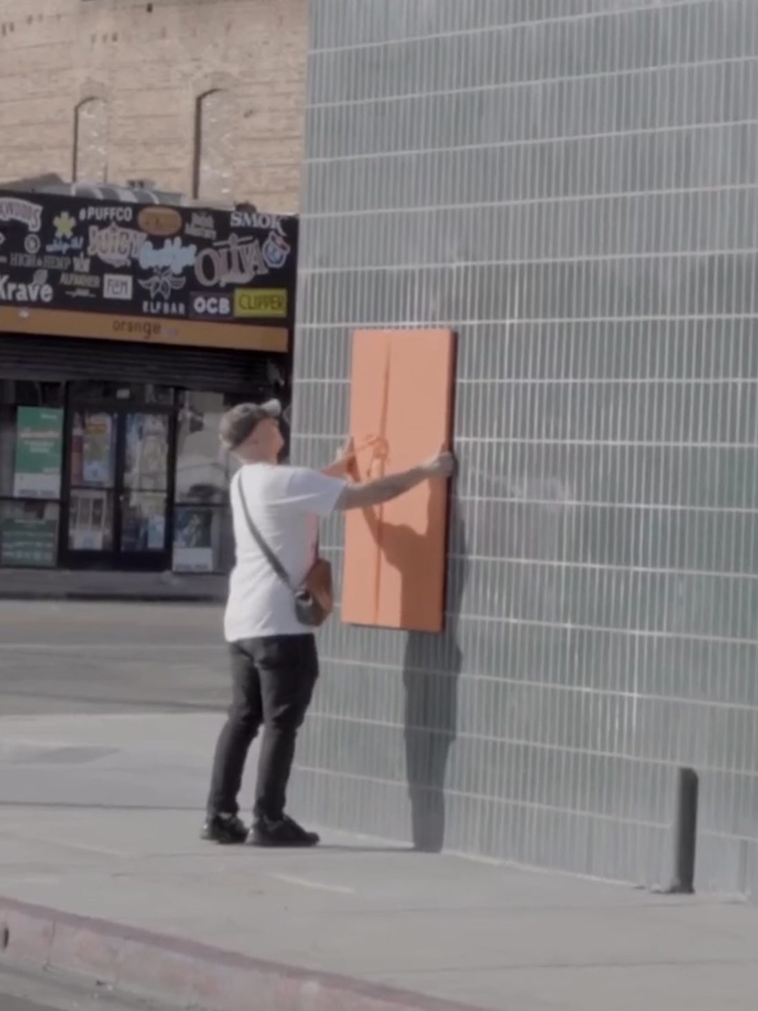 Matt Adam installing an orange-wrapped Unwrap and Steal artwork on a Los Angeles street wall