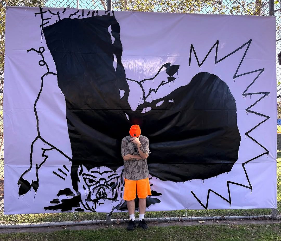 Matt Adam in an orange beanie standing in front of one of his large black-and-white paintings